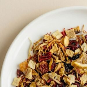 Close-up of CozySlip Mango Companion fruit tea blend on a white plate, featuring dried mango cubes, red berry pieces, and yellow flower petals, highlighting the natural and chunky texture of the loose leaf tea.