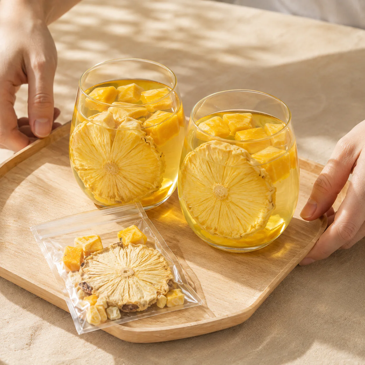 Two glasses of pineapple mango fruit tea with an individual pouch on a wooden tray