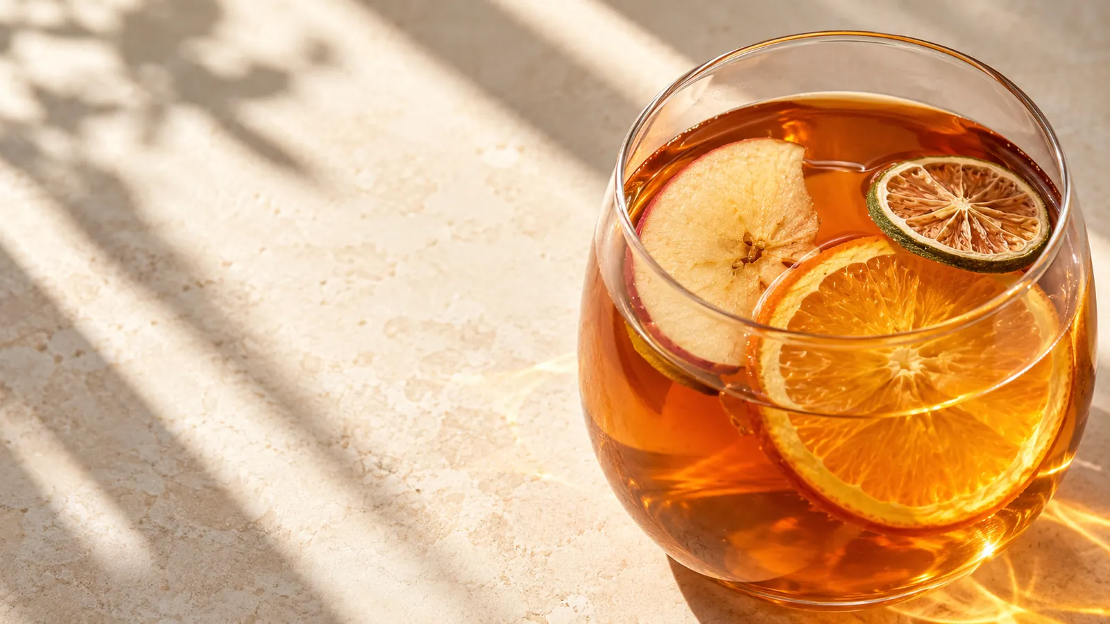 Overhead view of a clear glass of amber fruit tea casting a diagonal shadow